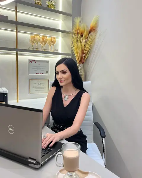 Hayane Melo sorrindo à mesa da clínica, com notebook e café